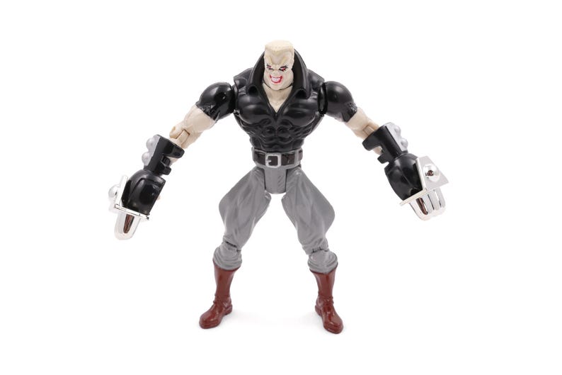 May include: A detailed action figure of a muscular character with a pale complexion, black top, gray pants, and red boots. The figure has large black gauntlets with silver accents and is posed with arms outstretched.
