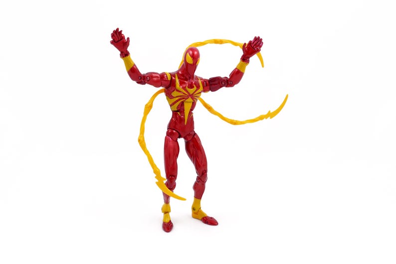 May include: Red and yellow action figure of a superhero with long, yellow, web-like appendages. The figure is posed with arms raised and legs spread.