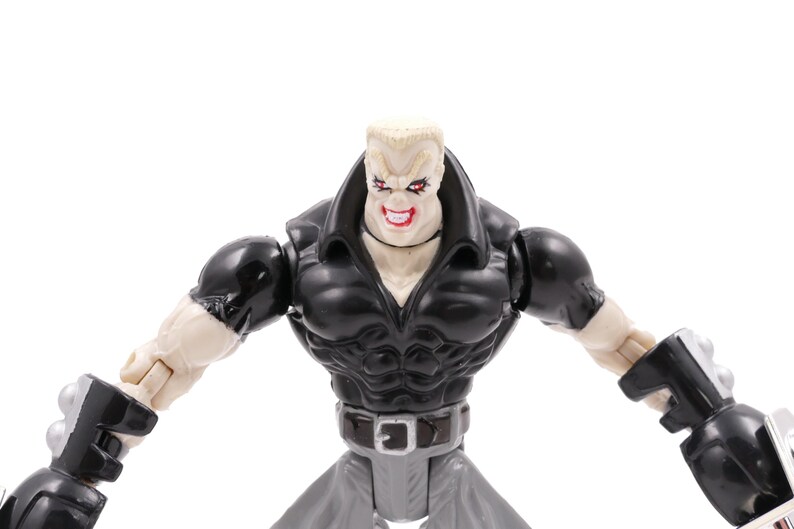 May include: A plastic action figure of a muscular character with a stern expression. The figure wears a black jacket, gray pants, and a silver belt. The figure's arms are outstretched, and it has a menacing grin.