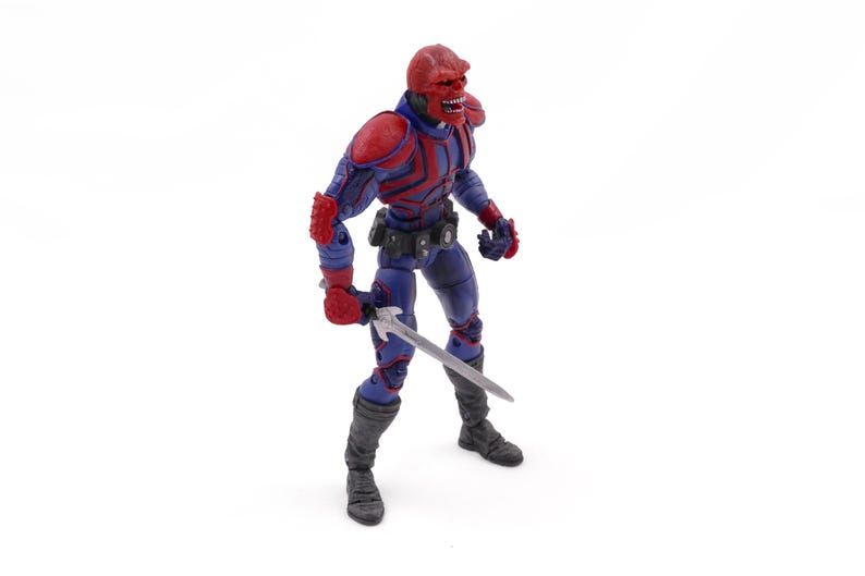 May include: A Red Skull action figure, featuring a red skull head, red and blue armor, and a silver sword. The figure is posed against a white background, showcasing its detailed design and menacing appearance. The figure is approximately 6 inches tall.