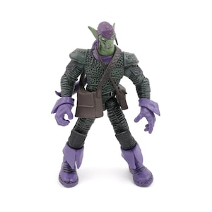 K&ouml;nnte beinhalten: Eine Green Goblin-Actionfigur mit lila Kapuze, Handschuhen und Stiefeln. Die Figur hat ein gr&uuml;nes Gesicht und ein dunkelgr&uuml;nes Outfit mit einer braunen Umh&auml;ngetasche. Die Figur steht auf einer wei&szlig;en Oberfl&auml;che.