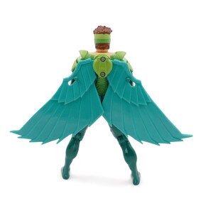 May include: A teal-winged action figure with a green and brown head and torso. The figure has a green body and legs, and the wings are spread out. The figure is standing on a white surface.