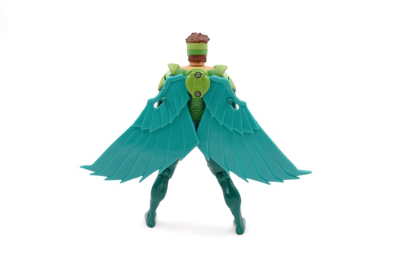 May include: A teal-winged action figure with a green and brown head and torso. The figure has a green body and legs, and the wings are spread out. The figure is standing on a white surface.
