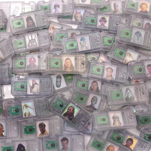 May include: A collection of clear plastic cases, each containing three small images of characters. The cases have a green circuit board design. The images feature characters from a science fiction franchise.