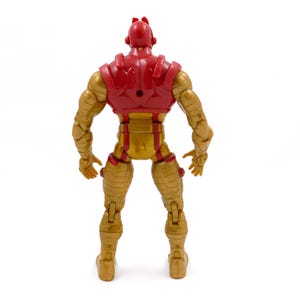 May include: Rear view of a red and gold action figure. The figure has a red helmet and chest piece, with gold-colored arms, legs, and torso. The figure is articulated and stands on a white surface.