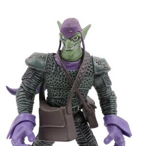 K&ouml;nnte beinhalten: Green Goblin Actionfigur mit lila Kappe, Handschuhen und Stiefeln. Die Figur hat einen finsteren Gesichtsausdruck und tr&auml;gt einen dunkelgr&uuml;nen Panzeranzug mit einer braunen Umh&auml;ngetasche. Sammlerst&uuml;ck.