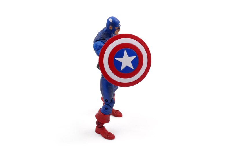 May include: A Captain America action figure in a blue and red suit, holding a shield with a white star on a blue circle, surrounded by red and white stripes. The figure is on a white background.