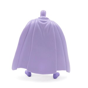 Puede incluir: Una figura de color lavanda de un personaje con capa. La figura se ve desde atr&aacute;s, mostrando el dise&ntilde;o fluido de la capa. La figura est&aacute; sobre un fondo blanco.