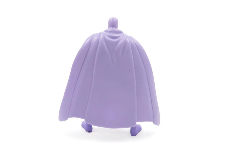 Puede incluir: Una figura de color lavanda de un personaje con capa. La figura se ve desde atr&aacute;s, mostrando el dise&ntilde;o fluido de la capa. La figura est&aacute; sobre un fondo blanco.