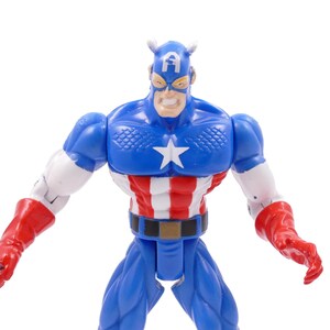 Pode incluir: Uma figura de a&ccedil;&atilde;o do Capit&atilde;o Am&eacute;rica em pose din&acirc;mica. A figura &eacute; predominantemente azul, com uma estrela branca no peito, listras vermelhas e brancas no torso e luvas vermelhas. A figura tem uma express&atilde;o severa e est&aacute; em um fundo branco.