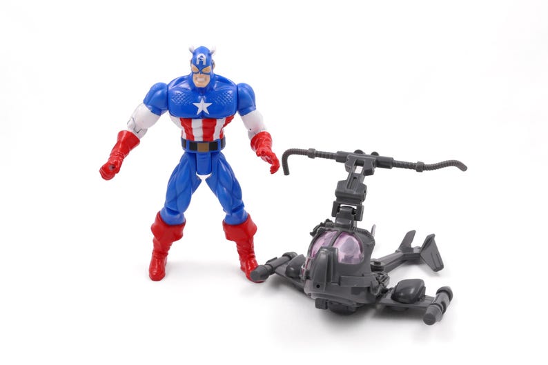 Pode incluir: Uma figura de a&ccedil;&atilde;o do Capit&atilde;o Am&eacute;rica em um traje cl&aacute;ssico azul, branco e vermelho est&aacute; ao lado de um helic&oacute;ptero de brinquedo cinza. A figura tem uma estrela no peito e um capacete. O helic&oacute;ptero tem um cockpit transparente.