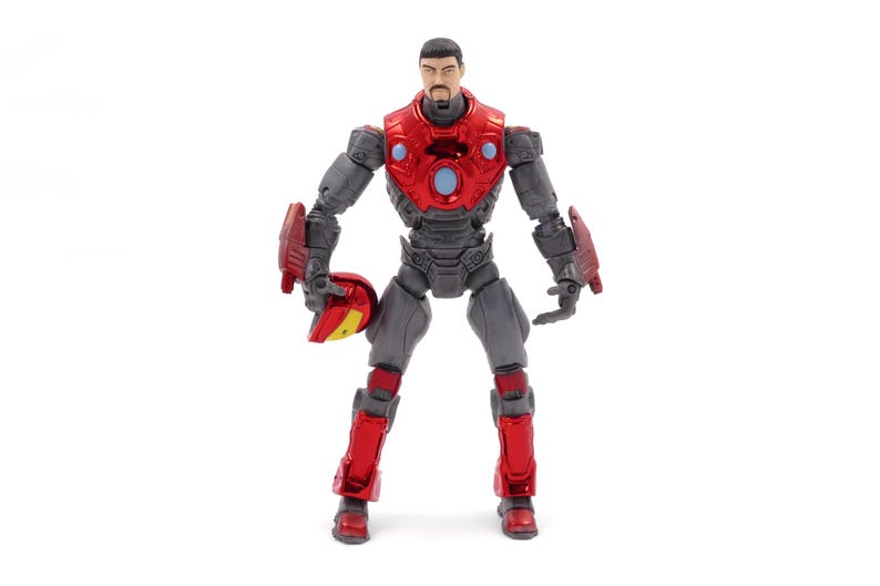 Op de afbeelding: Gedetailleerd actiefiguur van een superheld in een rood en grijs pantser. Het figuur houdt een helm vast en heeft een serieuze uitdrukking. Het figuur staat op een witte achtergrond. Het pantser van het figuur heeft een metallic glans.