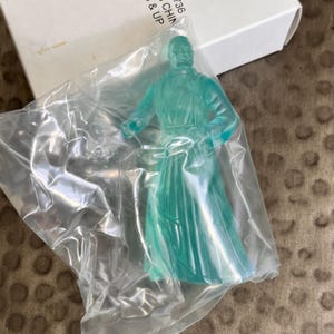 May include: A translucent green plastic action figure of a Jedi Master in a flowing robe. The figure is packaged in a clear plastic bag.