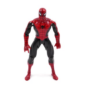 May include: A Spider-Man action figure in a standing pose. The figure is predominantly red and black, with a detailed web pattern on the red sections. The figure has a mask with white eye lenses.