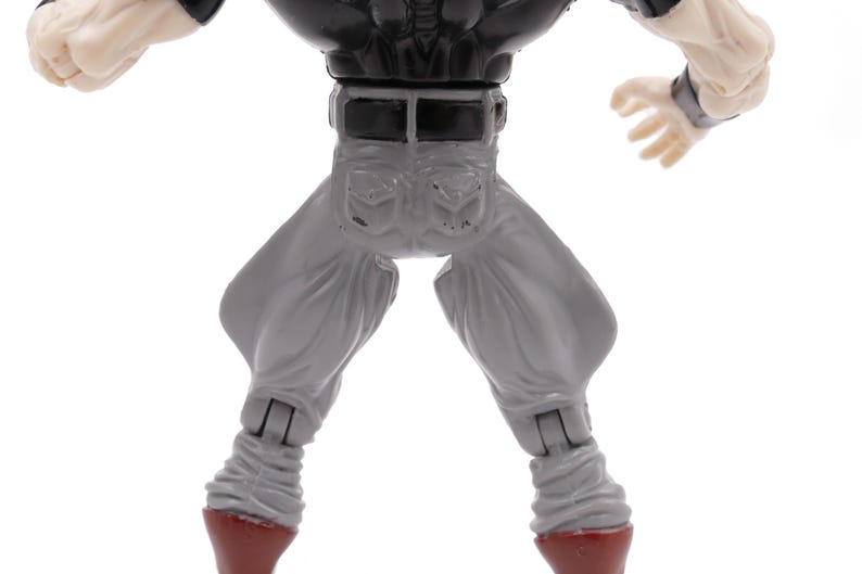 May include: A detailed view of a toy action figure, showcasing the lower torso and legs. The figure wears gray pants with a black belt and a black top. The figure's hands are visible, and the boots are red.