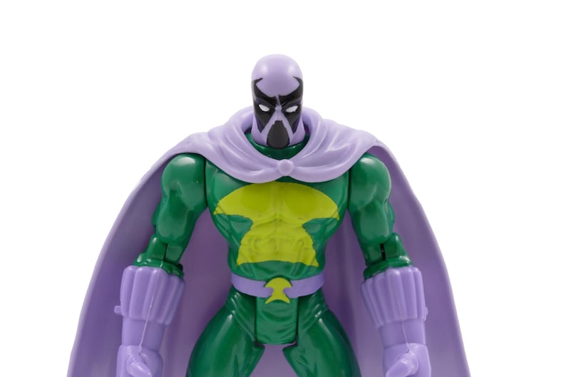 Puede incluir: Figura de acci&oacute;n verde con un emblema de pecho amarillo, capa morada y guantes a juego. La figura tiene una cara enmascarada con una cabeza morada y una m&aacute;scara negra. La figura es un superh&eacute;roe o un villano.