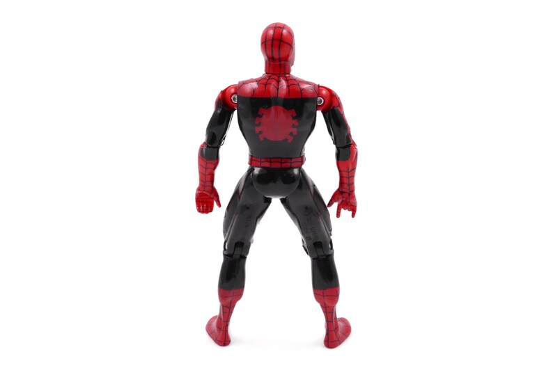 May include: A red and black action figure of a superhero, viewed from the back. The figure has a red head and hands, with a black body and legs. A red spider emblem is on the back. The figure is standing on a white surface.