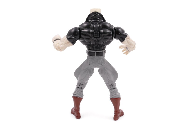 May include: A plastic action figure viewed from the back, featuring a black top, gray pants, and red boots. The figure has muscular arms and a neutral skin tone. The figure is posed with arms raised.