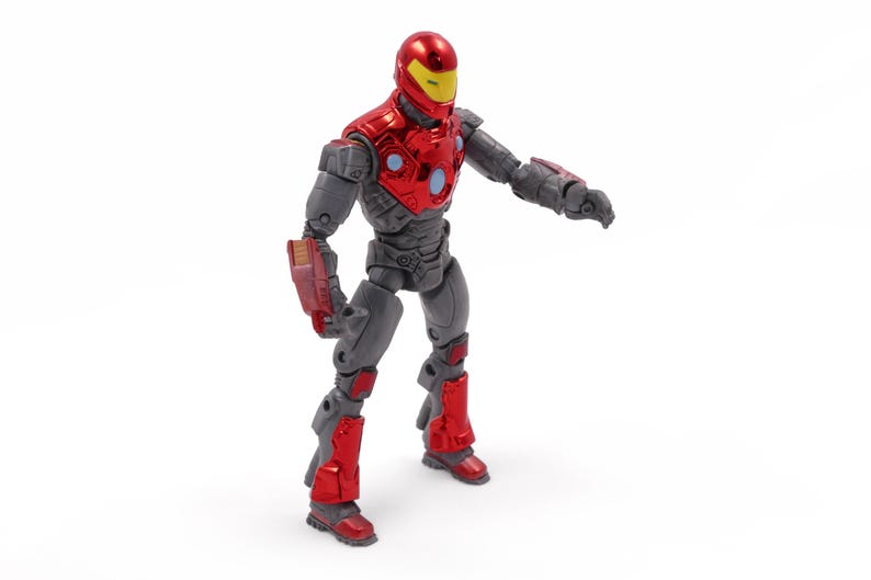 Op de afbeelding: Een rood en grijs actiefiguur van een superheld met een helm en harnas. Het figuur heeft een rode helm met een gele vizier, rode borstpantsering en rode accenten op de benen en armen. Het figuur staat met &eacute;&eacute;n arm uitgestrekt.