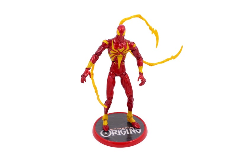 May include: Red and yellow action figure of Spider-Man with web shooters. The figure is standing on a red base with the words "Spider-Man Origin" printed on it.