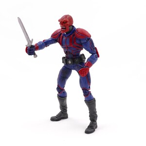 May include: A Red Skull action figure in a dynamic pose, holding a silver sword. The figure is clad in a blue and red costume with black boots and a utility belt. The figure has a red skull-like head.
