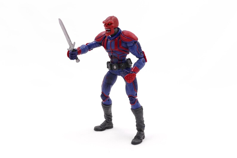 May include: A Red Skull action figure in a dynamic pose, holding a silver sword. The figure is clad in a blue and red costume with black boots and a utility belt. The figure has a red skull-like head.