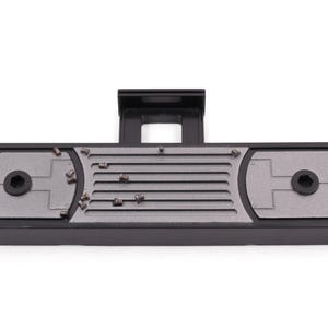 May include: A black and gray rectangular device with a raised section and a central slotted area. The device has two circular areas with a hexagonal center and several small, metallic objects scattered across the surface.