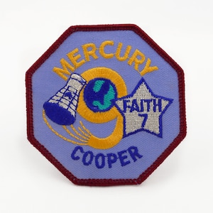 May include: A blue and gold embroidered patch with the text "MERCURY 9 COOPER" and a silver star with the text "FAITH 7".
