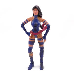 May include: A posable action figure with long dark hair, wearing a dark blue bodysuit with matching arm and leg bands. The figure features a red sash tied around the waist, exposed skin on the arms and legs, and dark blue boots on a white background.