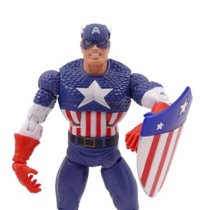 K&ouml;nnte beinhalten: Captain America Actionfigur, mit einem blauen und wei&szlig;en Stern auf der Brust, einem blauen Helm mit einem wei&szlig;en "A" und einem Schild mit roten und wei&szlig;en Streifen. Die Figur tr&auml;gt einen blauen Anzug mit roten Handschuhen.
