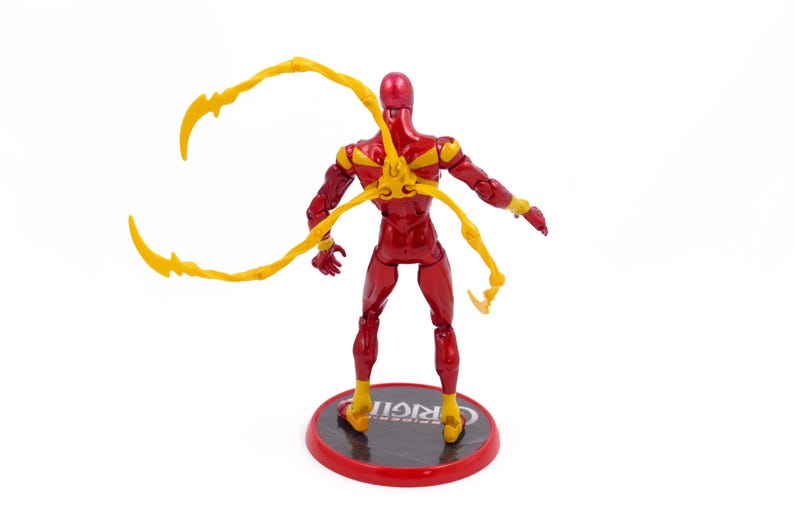 May include: Red and yellow action figure with four articulated arms. The figure is standing on a black base with the word "ORIGIN" printed on it.