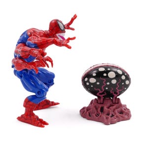 May include: A red and blue Spider-Man action figure with multiple arms and a menacing expression. Beside it is a black and white egg-shaped object on a purple base. The toy is likely a collectible.