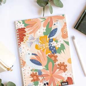 May include: A spiral bound notebook with a floral design featuring two birds. The notebook has a peach background with pink, orange, yellow, green, and blue flowers. The text "Step by step, Day by day" is printed on the cover. The notebook is made by SEIK.