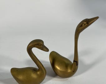 Può includere: Due piccole statuine di cigno in ottone. I cigni sono rivolti in direzioni diverse e hanno una finitura liscia e lucida.