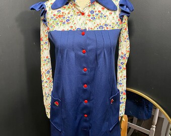 May include: A blue and white dress with a floral print and red buttons. The dress has a collar and long sleeves.