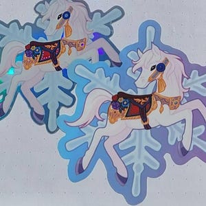 May include: Two stickers featuring a white carousel horse with a detailed saddle and gold accents. The horse is set against a blue and silver snowflake background. The stickers have a holographic effect.