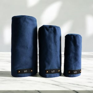 May include: Three navy blue golf club head covers of varying heights, each featuring a rectangular black leather patch at the base with the letters LC embossed in white and secured by two small metallic rivets on the left and right sides.