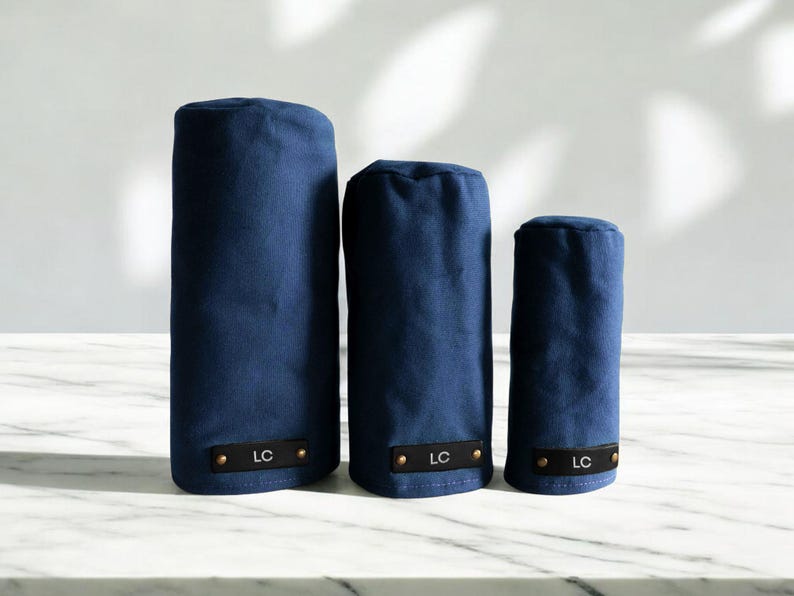 May include: Three navy blue golf club head covers of varying heights, each featuring a rectangular black leather patch at the base with the letters LC embossed in white and secured by two small metallic rivets on the left and right sides.