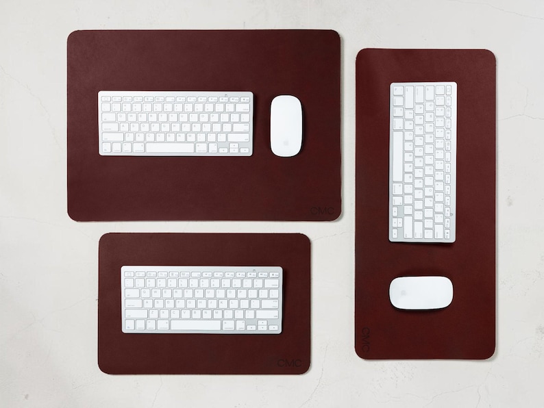May include: A collection of three burgundy-colored desk mats with white keyboards and mice. The mats are rectangular, with rounded corners. The keyboards and mice are positioned on the mats, ready for use. The setup is clean and modern.