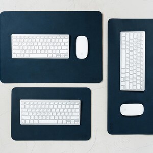 May include: Three dark blue rectangular desk pads with rounded corners. Each pad has a white keyboard and a white mouse. The pads are arranged on a light-colored surface. The bottom right corner of each pad has the letters "BGR".