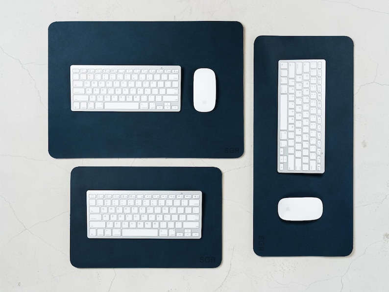 May include: Three dark blue rectangular desk pads with rounded corners. Each pad has a white keyboard and a white mouse. The pads are arranged on a light-colored surface. The bottom right corner of each pad has the letters "BGR".