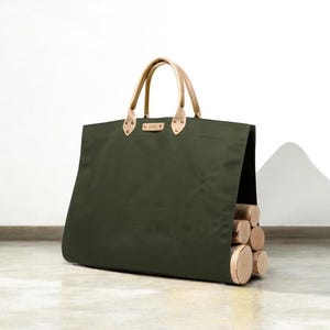 May include: An olive green canvas tote bag with tan leather handles and accents. The bag is filled with several cut logs. The bag is designed for carrying firewood.