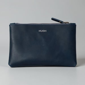 Pode incluir: Uma bolsa de couro azul marinho com fecho de correr e uma pequena aba. A palavra "HUGH" est&aacute; gravada em prata na frente. A bolsa &eacute; retangular e parece estar vazia. Ideal para guardar pequenos objetos.