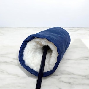 May include: A navy blue golf club headcover featuring a thick, white, plush faux-shearling interior lining. The cylindrical cover is constructed from a durable, solid-colored fabric and is shown with a black golf club shaft extending from the center.