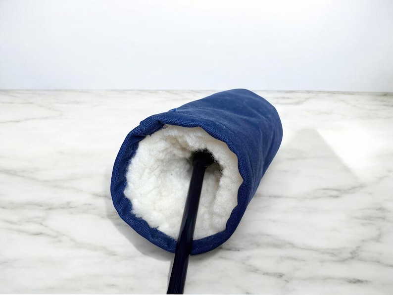 May include: A navy blue golf club headcover featuring a thick, white, plush faux-shearling interior lining. The cylindrical cover is constructed from a durable, solid-colored fabric and is shown with a black golf club shaft extending from the center.