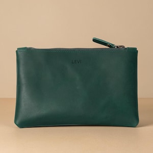 Pode incluir: Uma bolsa de couro verde escuro com fecho de correr e uma pequena aba. A palavra "LEVI" est&aacute; sutilmente gravada na frente. A bolsa &eacute; retangular e est&aacute; sobre uma superf&iacute;cie neutra.