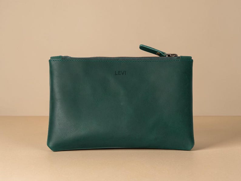 Pode incluir: Uma bolsa de couro verde escuro com fecho de correr e uma pequena aba. A palavra "LEVI" est&aacute; sutilmente gravada na frente. A bolsa &eacute; retangular e est&aacute; sobre uma superf&iacute;cie neutra.