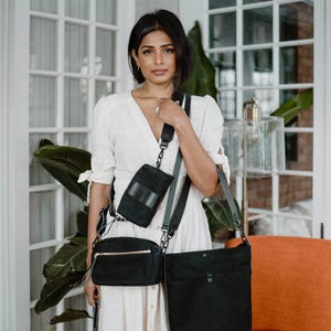 Puede incluir: Un conjunto de bolsos de lona negra que incluye un bolso grande, un bolso bandolera rectangular con cremallera dorada, una bolsa vertical pequeña y un bolso accesorio diminuto, con herrajes en color negro.