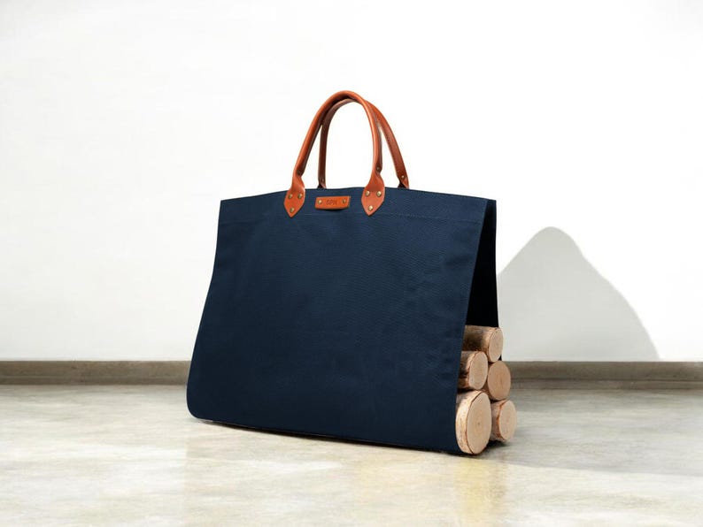 May include: A navy blue tote bag with brown leather handles and accents. The bag is filled with several logs. The bag is designed for carrying firewood. The bag is made of a durable material.