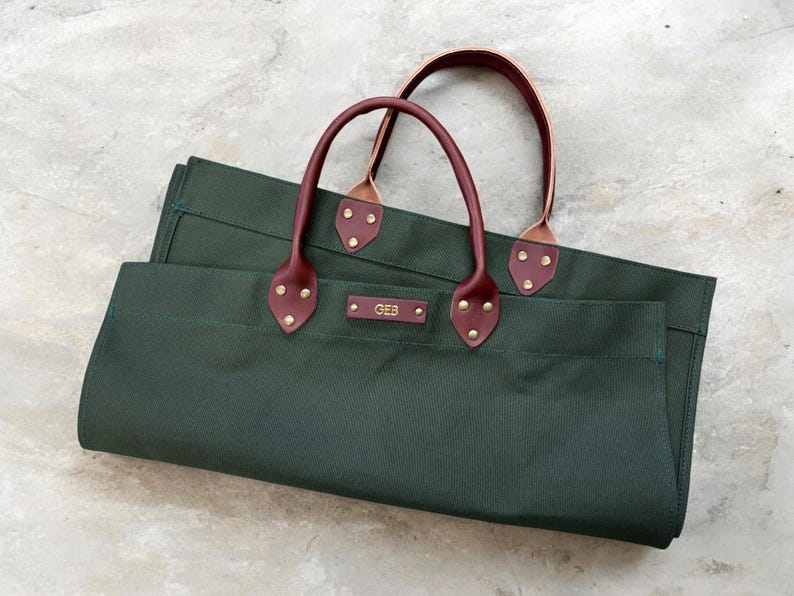 May include: Two dark green canvas tote bags with burgundy leather handles and accents. The handles are attached with brass rivets. The bags have a rectangular shape and a small rectangular tag with the initials "GEB".
